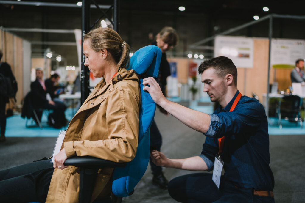 Une femme est assise dans un siège professionnel bleu, l'exposant adapte les réglages du siège.
