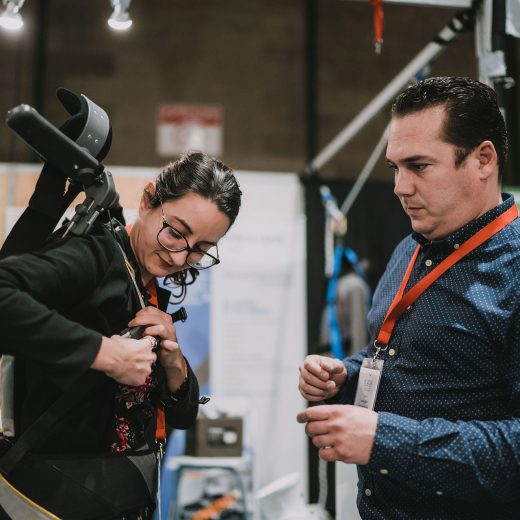 Une femme essaye un équipement professionnel de port de charge, face à l’exposant qui l’aide à s’équiper Une femme essaye un équipement professionnel de port de charge, face à l'exposant qui l'aide à s'équiper