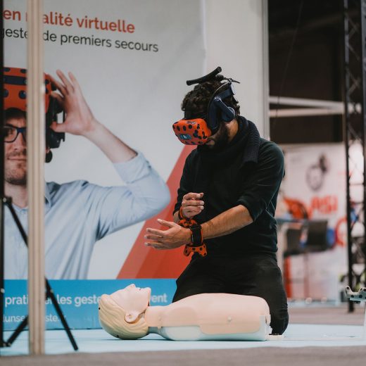 Un homme fait des gestes de premier secours sur un mannequin, équipé de lunettes de réalité virtuelle et de capteurs aux poignets