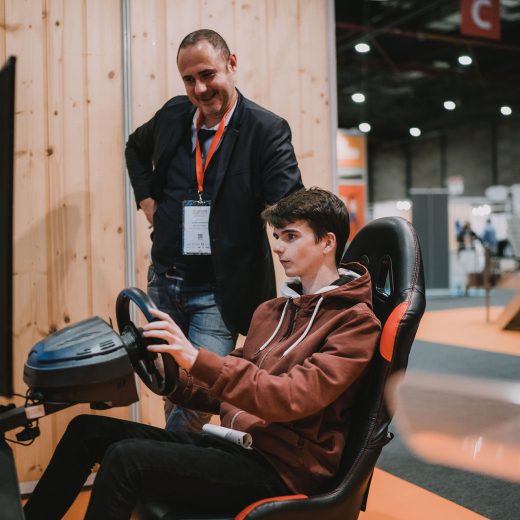 Un jeune homme fait de la conduite en simulation sur un écran avec l’exposant à côté de lui Un jeune homme fait de la conduite en simulation sur un écran avec l'exposant à côté de lui